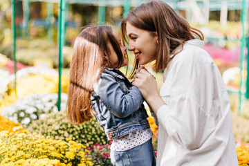 Young woman in white shirt enjoying life with child. Outdoor photo of kid and mother posing beside...
