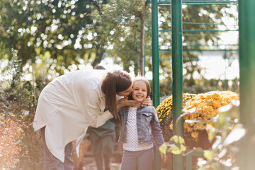 Woman in white shirt kissing daughter in sunny day. Outdoor shot of mother expressing love to child in park.