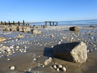 A view of the beach and the sea and numerous remnants of concrete and metal - A beach with a mess
