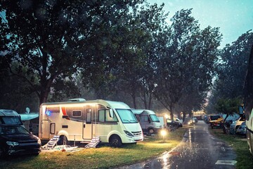 Campsite during a rainy evening. Sun already set so sky is getting darker and darker. Cars and campervan turned on their lights which beautifully spark on wet road
