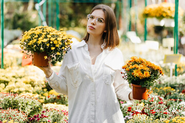 Pensive young woman posing in garden. Attractive girl in glasses holding flower pots.