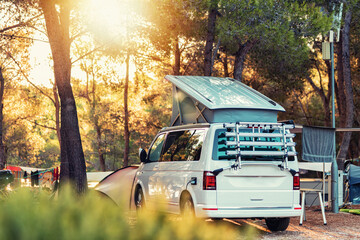 Campervan caravan vehicle for van life holiday on mobile home camper mobile motor home. Golden sunshine sneaking through sparse trees of camping. Roof of campervan is covered in colourful sunshine - obrazy, fototapety, plakaty