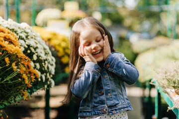 Blithesome child in denim jacket posing near flowers. Laughing kid enjoying life.