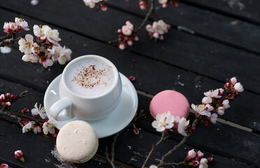 Cup of hot  coffee with macaroon cookies and spring flowers on the old rustic black wooden tabletop.