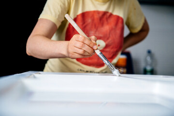 Focus on the hand of pregnant woman doing painter job renovation of old wooden window frame painting it with white acrylic paint