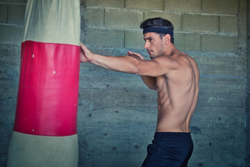 A handsome young man practicing boxing on a punching bag