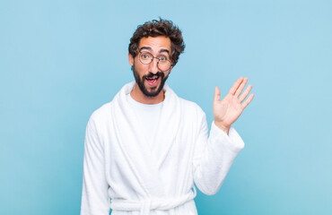 young bearded man wearing a bath robe smiling happily and cheerfully, waving hand, welcoming and...