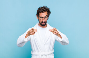 young bearded man wearing a bath robe pointing forward at camera with both fingers and angry...