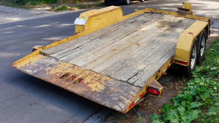 Rear view of weathered empty flatbed trailer parked on street in residential neighborhood.