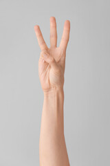 Hand showing letter W on grey background. Sign language alphabet
