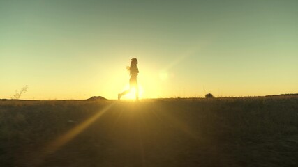 running after sun. training jogging. healthy beautiful girl is engaged in fitness, jogging in country in sun. Jogger girl breathes fresh air on field. Free young woman runs in summer park at sunset.