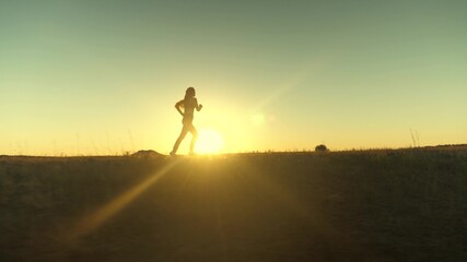 running after sun. training jogging. healthy beautiful girl is engaged in fitness, jogging in country in sun. Jogger girl breathes fresh air on field. Free young woman runs in summer park at sunset.