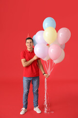 Young man with balloons and party hat on color background