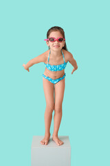 Little girl in start position on swimming block against color background