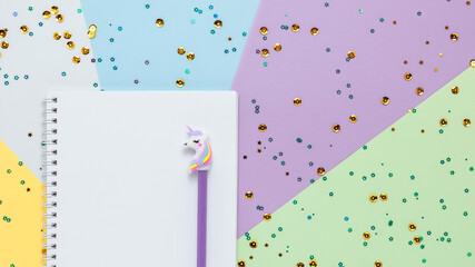 Notebook and pencil with unicorn on colors paper with glitter stars and sequins flat lay pastel background. Festive and celebration concept. © valeriyakozoriz