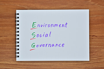 A sketchbook with "Environment, Social, Governance" written on it is placed diagonally on a wooden board.