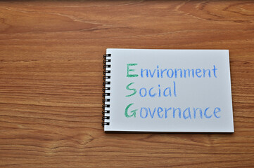 A sketchbook with "Environment, Social, Governance" written on it is placed diagonally on a wooden board.