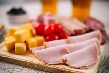 Selección de fiambres en tabla de madera de lomo ahumado, lomo cocido, jamón cocido, queso, salame de milán, acompañado de aceitunas y cerveza