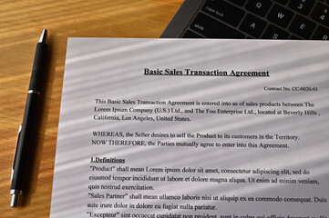 The "Basic Sales Transaction Agreement" is placed on a laptop on my desk.