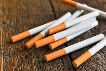 A close up image of several loose cigarettes on a dark wooden table top. 