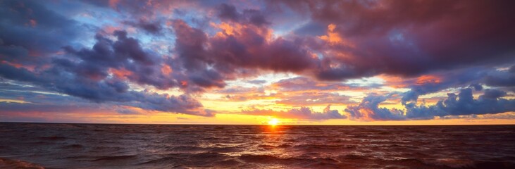Epic dark sunset sky above the sea shore after the storm. Dramatic glowing colorful red clouds,...
