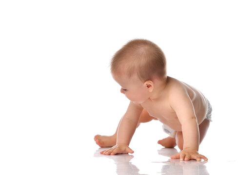 Portrait of a sweet cute baby toddler in diapers barefoot, crawling on the floor and looking at something on a white background in the studio, side view.