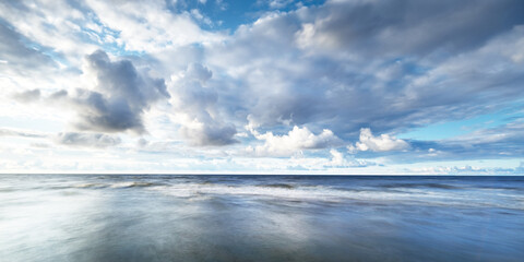 Clear sky with lots of glowing cumulus clouds above the Baltic sea shore after thunderstorm at sunset. Dramatic cloudscape. Picturesque scenery. Fickle weather, climate change. Long exposure