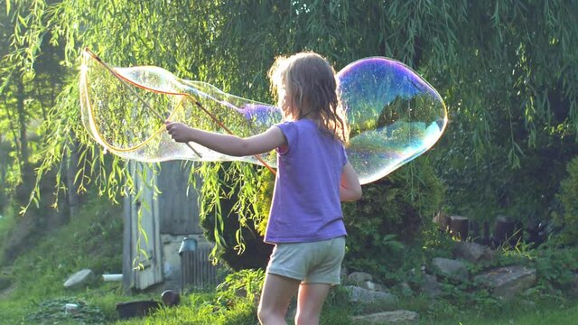 Young Girl Playing with Giant Soap Bubbles at Sunset Backlit View 