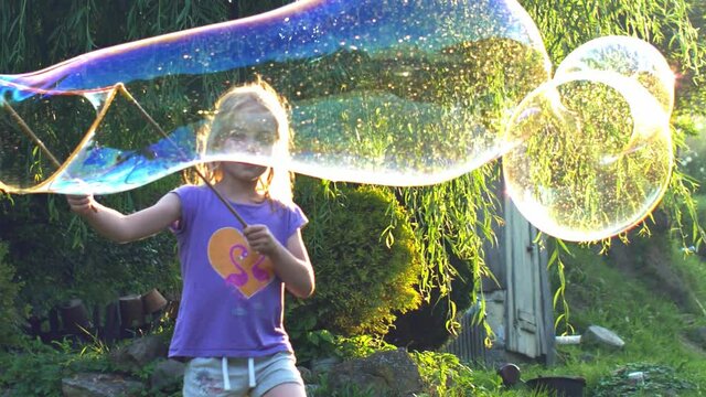 Young Girl Playing with Giant Soap Bubbles at Sunset Backlit View 