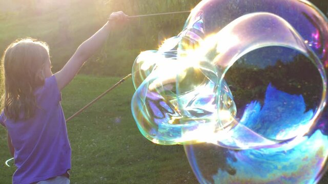 Young Girl Playing with Giant Soap Bubbles at Sunset Backlit View 