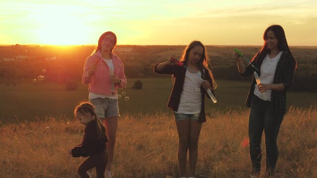 healthy children and mom play, blow kid catches soap bubbles. mother and sisters play together in park at sunset. Happy family and childhood concept. blow bubbles in sun, children's birthday