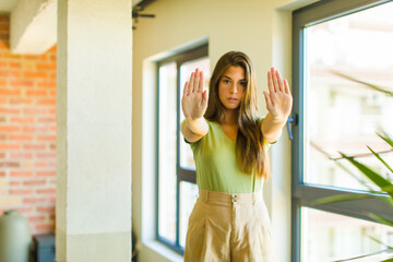 young pretty woman looking serious, unhappy, angry and displeased forbidding entry or saying stop...