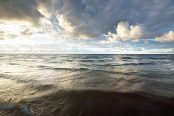 Clear sky with lots of glowing cumulus clouds above the Baltic sea shore after thunderstorm at sunset. Dramatic cloudscape. Warm golden sunlight. Picturesque scenery. Fickle weather. Long exposure