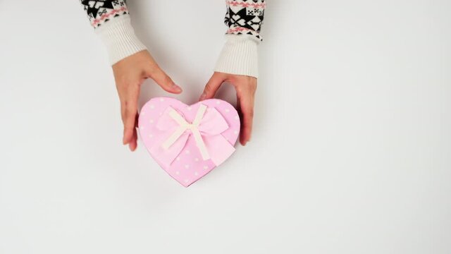 baked round multi-colored macarons in a heart-shaped pink cardboard box, female hands take dessert, top view