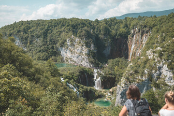 Group of tourists walking in Plitvice Lakes National Park on wood bridge in forest. Young tall...