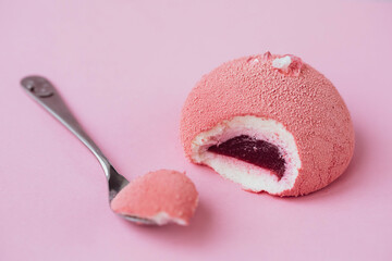 Modern european dessert with piece of it on tea spoon on colored pink background. Mini mousse cake topped with pink glaze and decorated with culinary gel drops. creative minimalism concept, copy space