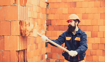 Adult handsome worker builder using hammer and smash tool at construction site. Man using sledge-hammer. Labor are using hammer smash destroy cement wall.
