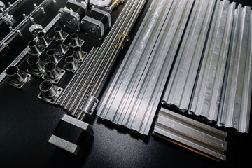 a set of parts for a laser machine on a black background, silver backlight, flat lay arduino board for controlling the machine and v slot aluminum profile lies .