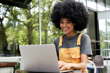 Happy hipster African American female student, freelancer with Afro hair using laptop computer...