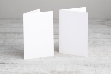 Two white greeting cards mockup, standing upright on a white wooden desk. Blank closed cards template. 