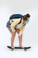 Naklejka premium Vertical photo of a barefoot teen girl with the masks on the face and a backpack rolling on the skate board over the white background