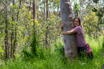 Naklejka na ściany i meble Real woman in hippie attitude hugging a tree in the middle of the forest.