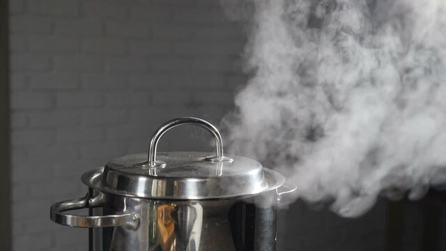Steam or Vapour clouds rising from boiling water in saucepan on stove. Steam from pan while cooking. Cooking process in slow motion. Steam and white smoke rising on dark background. Full hd