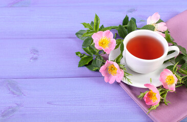 Fototapeta na wymiar Cup of tea and wild rose flower on purple boards, copy space for text