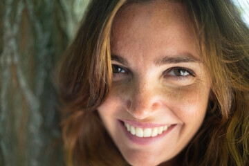 Close-up portrait of southern Italian woman with long brown wavy hair standing outdoors in the countryside with elegant pose and bright smile