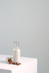 Almond milk in a glass bottle and pile of roasted almonds on white table against white wall.