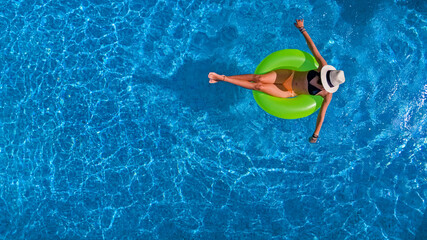 Beautiful woman in hat in swimming pool aerial view from above, young girl in bikini relaxes and swims on inflatable ring donut and has fun in water on vacation
