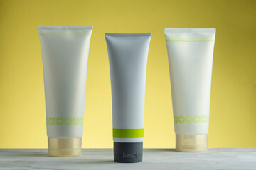 Envases de crema blancos para publicidad, sobre una base de mármol y fondo amarillo.