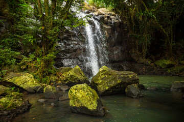 Naklejka na ściany i meble Waterfall landscape. Beautiful hidden waterfall in tropical rainforest. Foreground with big stones. Fast shutter speed. Sing Sing Angin waterfall, Bali, Indonesia
