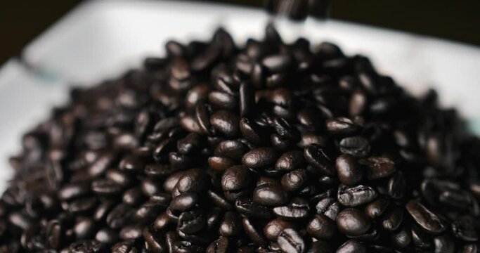 Dark roasted coffee beans falling into a pile.